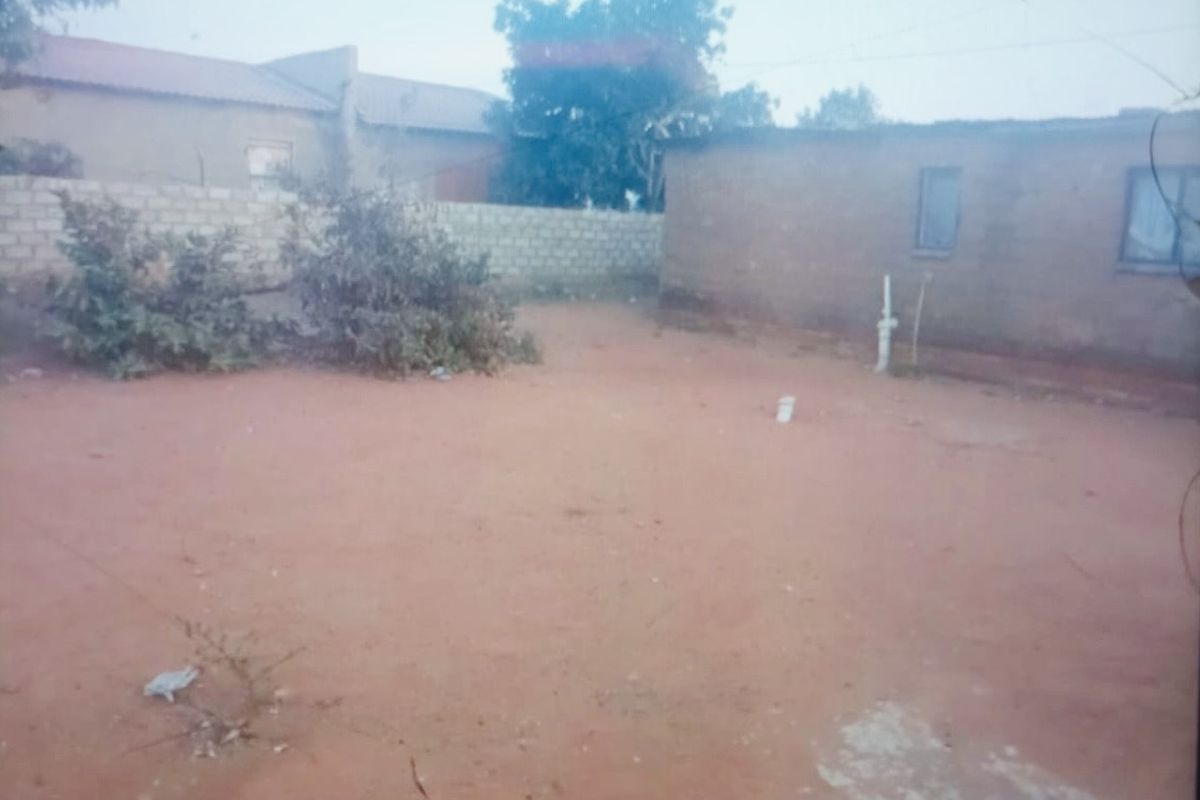 A view of the rear exterior area featuring an unpaved yard, perimeter walling, and basic building structure.