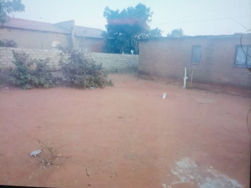 A view of the rear exterior area featuring an unpaved yard, perimeter walling, and basic building structure.