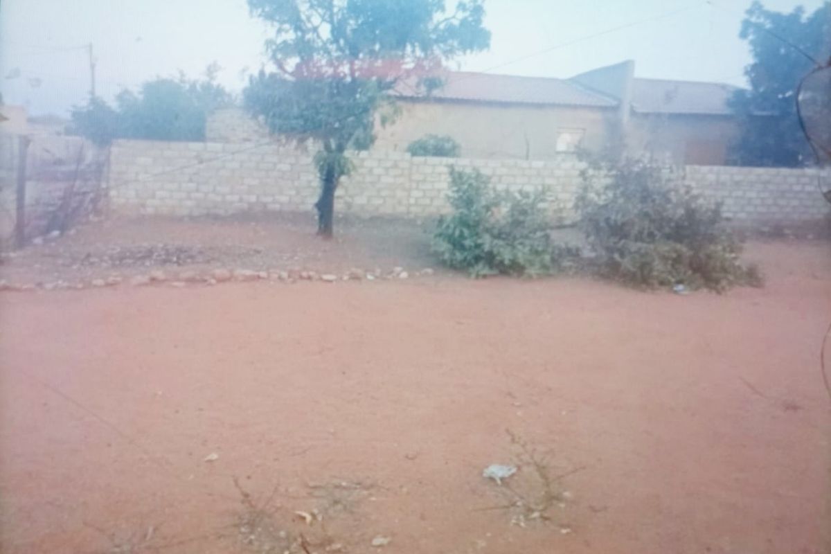 A view of the property's rear exterior, featuring an unpaved yard area and a perimeter boundary wall.