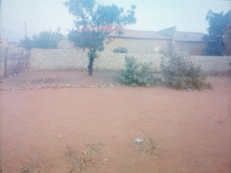 A view of the property's rear exterior, featuring an unpaved yard area and a perimeter boundary wall.