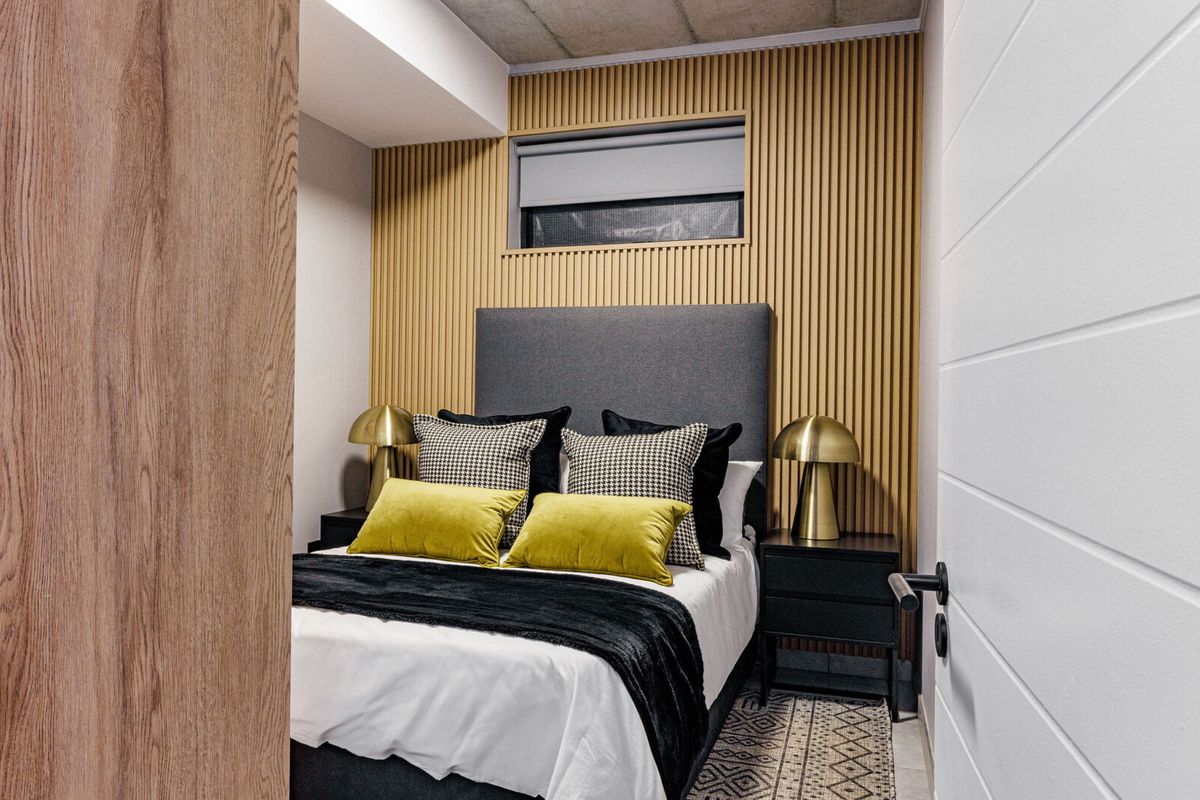 A modern, well-appointed bedroom featuring a textured wood-slat feature wall, exposed concrete ceiling, and a high-set window for natural light.