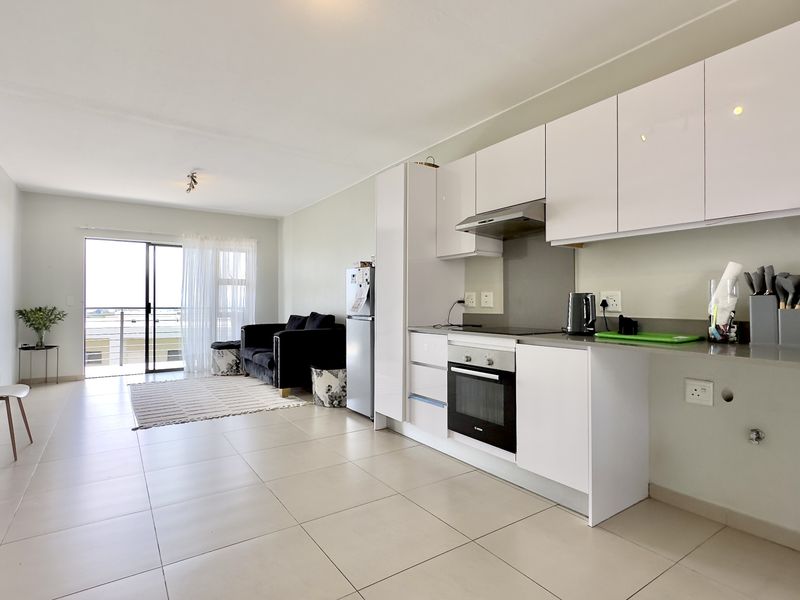 Modern open-plan apartment featuring a sleek kitchen with built-in appliances, tiled flooring, and seamless access to a private balcony.