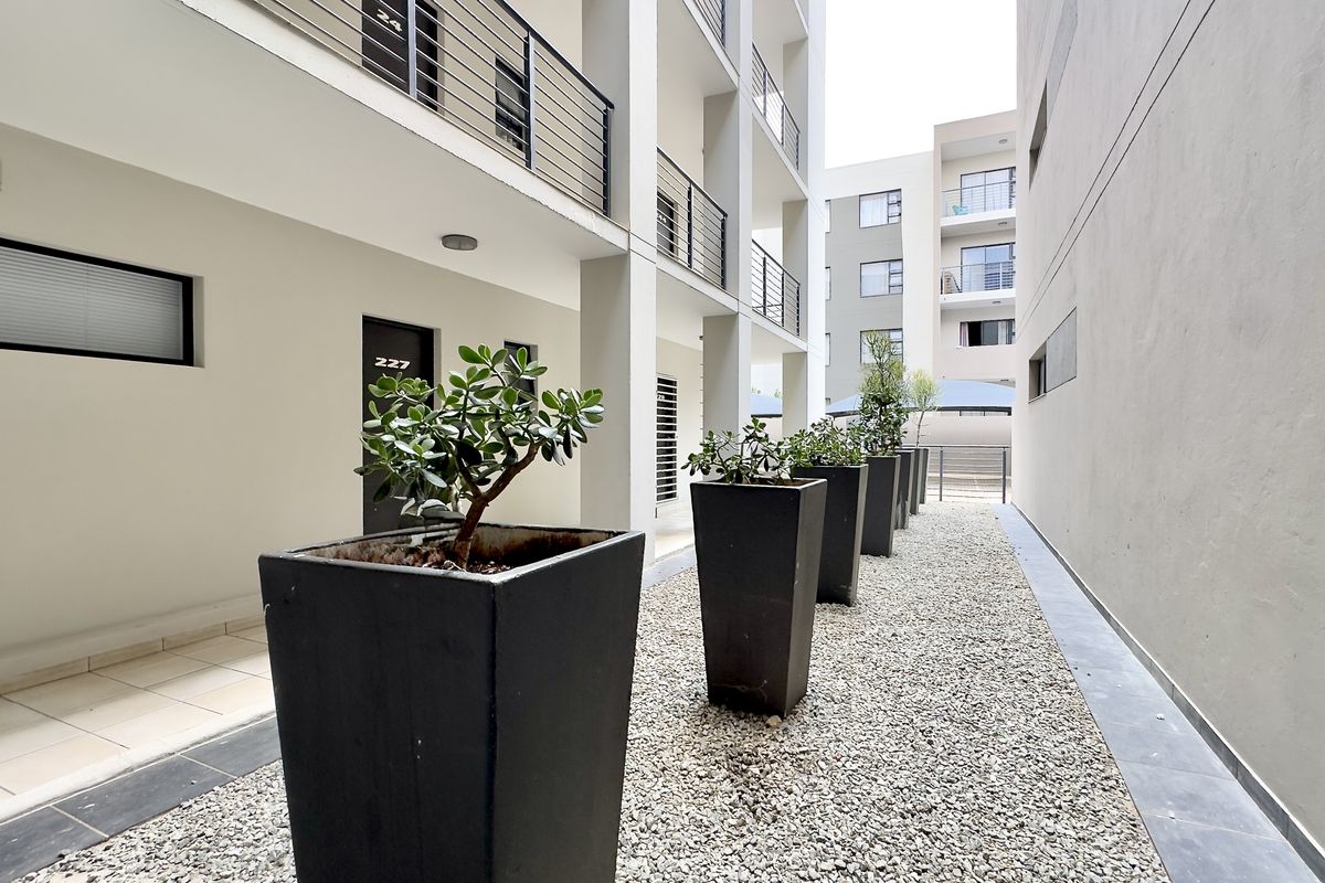 A well-maintained exterior walkway between apartment blocks featuring gravel landscaping, modern metal railings, and clean building facades.