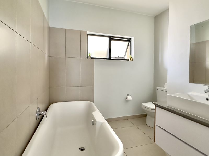 A modern, well-maintained bathroom featuring a bathtub, wall-mounted basin with vanity storage, toilet, and neutral tiled finishes.
