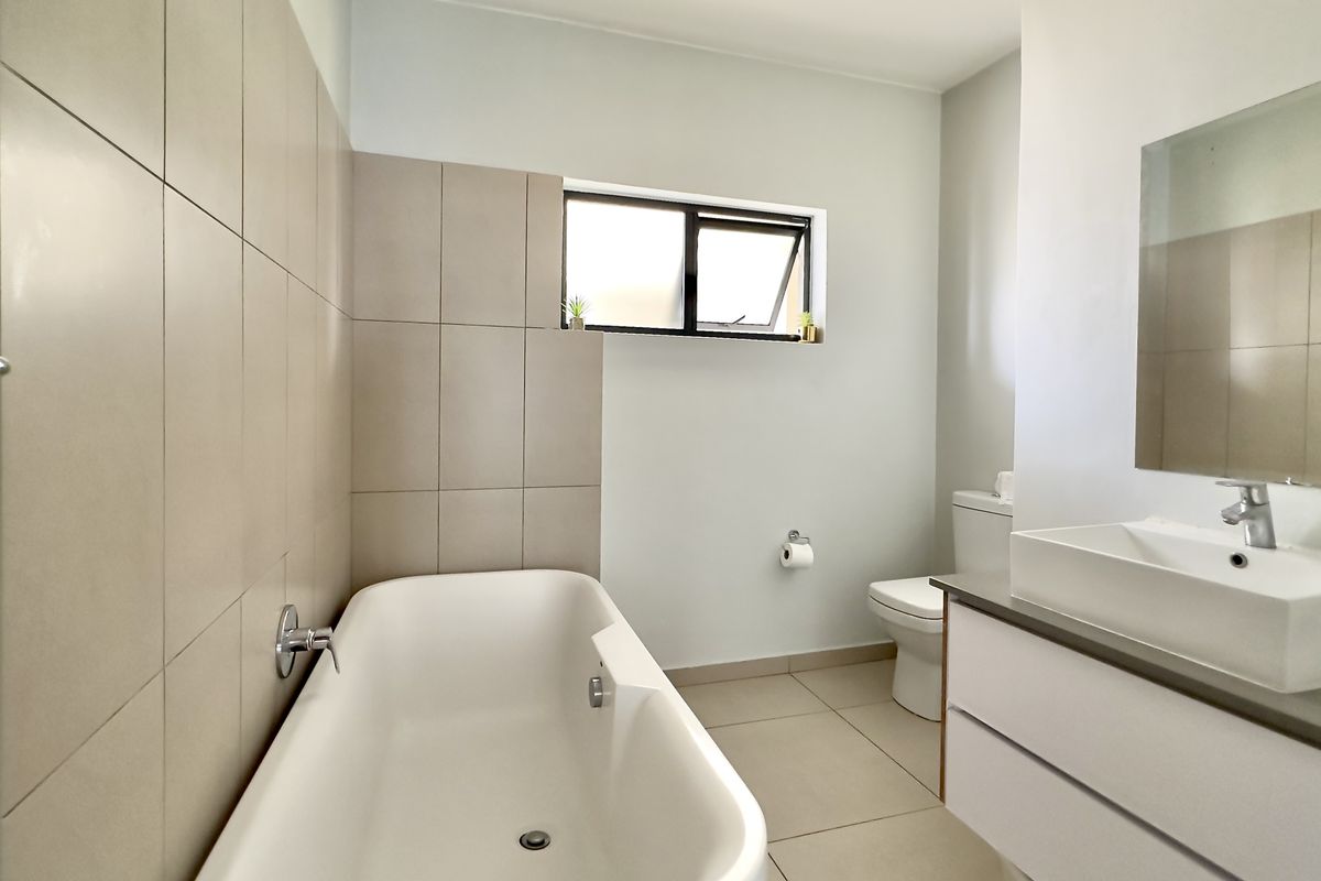 A modern, well-maintained bathroom featuring a bathtub, wall-mounted basin with vanity storage, toilet, and neutral tiled finishes.
