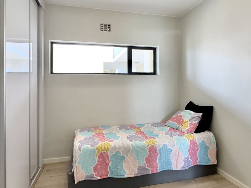 A clean, modern bedroom featuring light-toned flooring, a built-in wardrobe with sliding mirror doors, and a horizontal window for natural light.