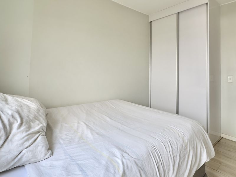 A clean bedroom featuring light-toned laminate flooring and a functional built-in sliding door wardrobe, offering a neutral and well-maintained living space.