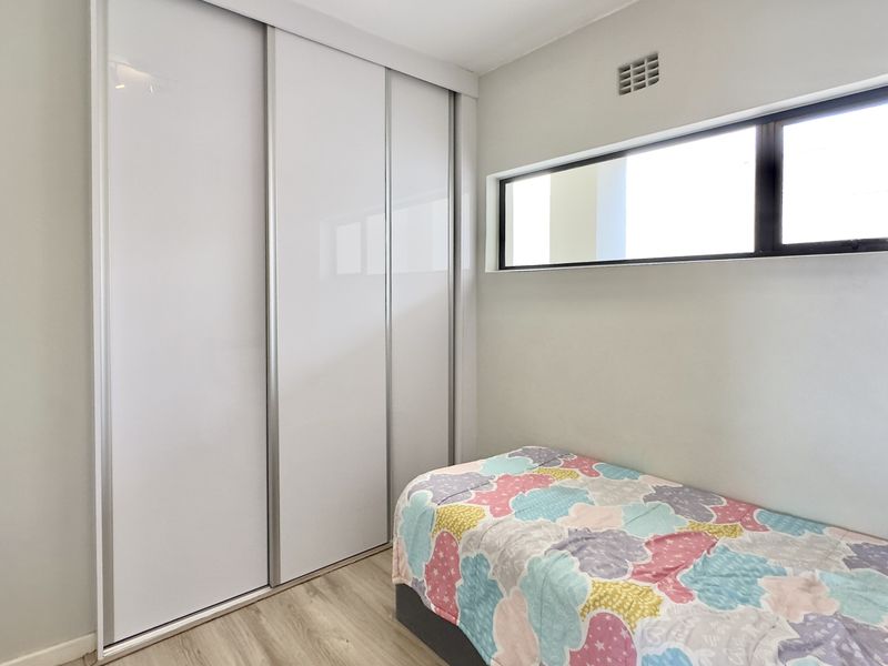 A bright bedroom featuring modern laminate flooring, a built-in sliding door wardrobe, and a high-level horizontal window for natural light.