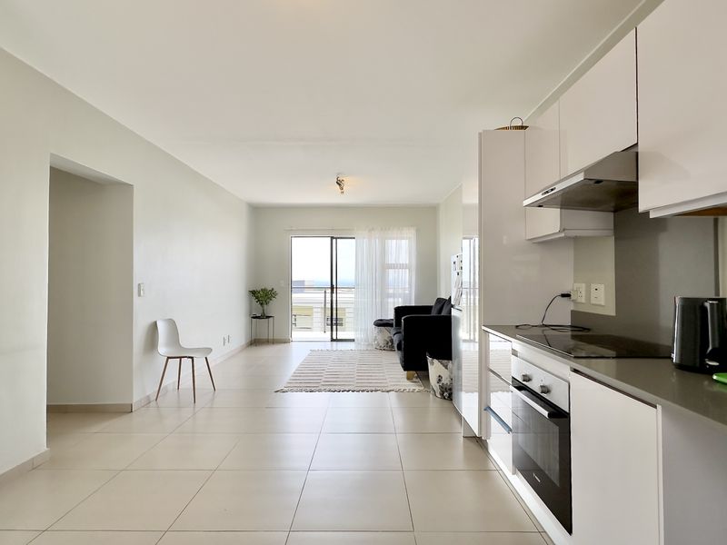 Modern open-plan living area featuring a sleek kitchen with built-in appliances, tiled flooring, and seamless access to a balcony with natural light.