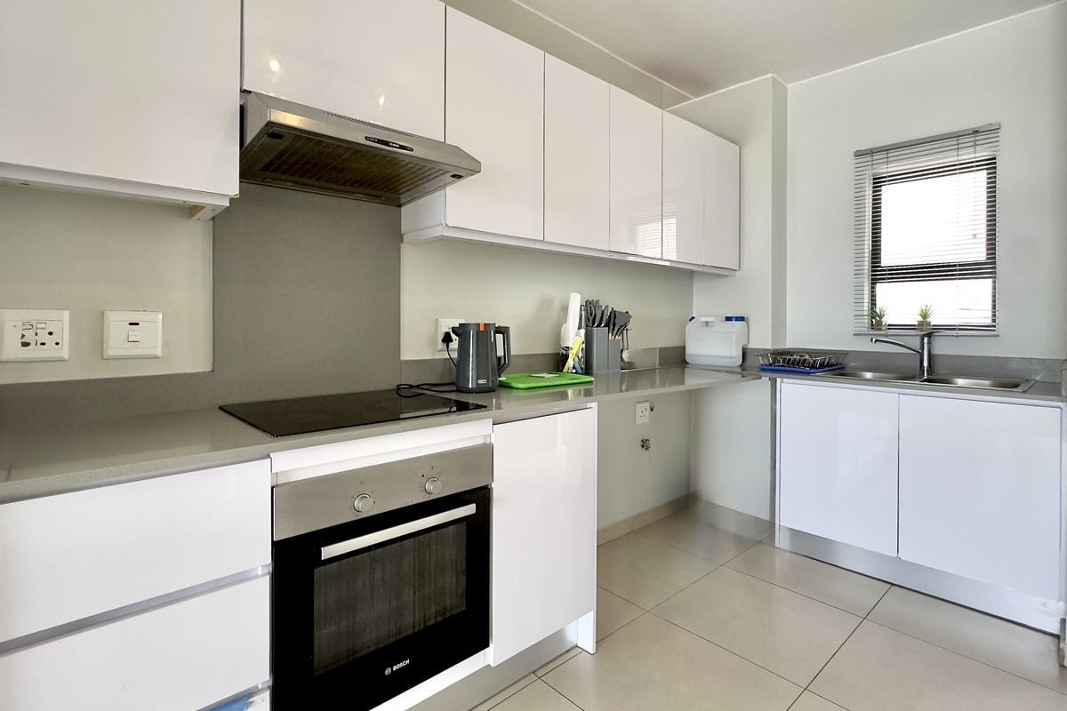 Modern kitchen featuring white gloss cabinetry, stone countertops, integrated electric hob, oven, extractor fan, and a stainless steel sink with tiled flooring.