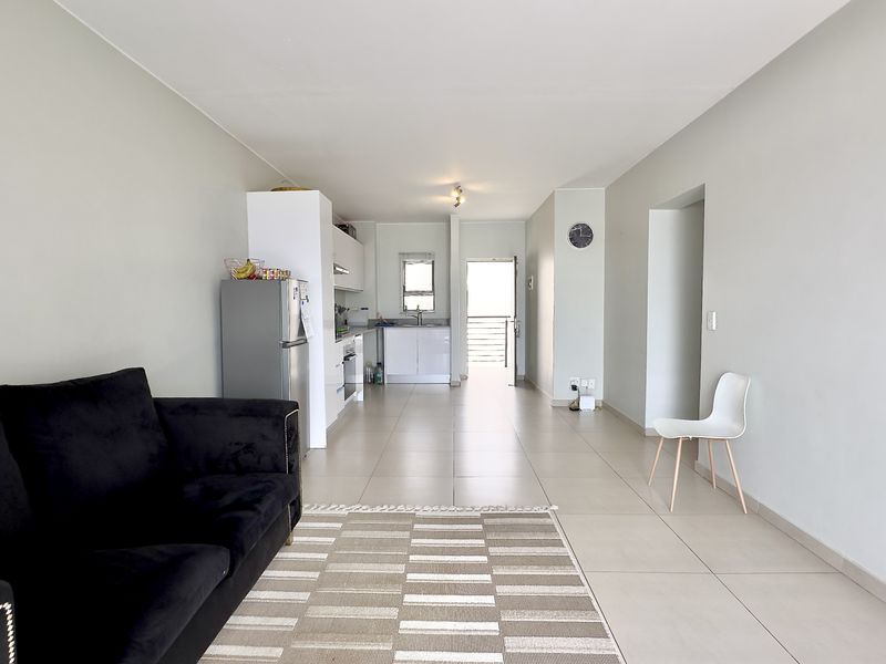 Open-plan living area featuring tiled floors and a functional kitchen with built-in cabinetry, leading towards an exterior balcony entrance.