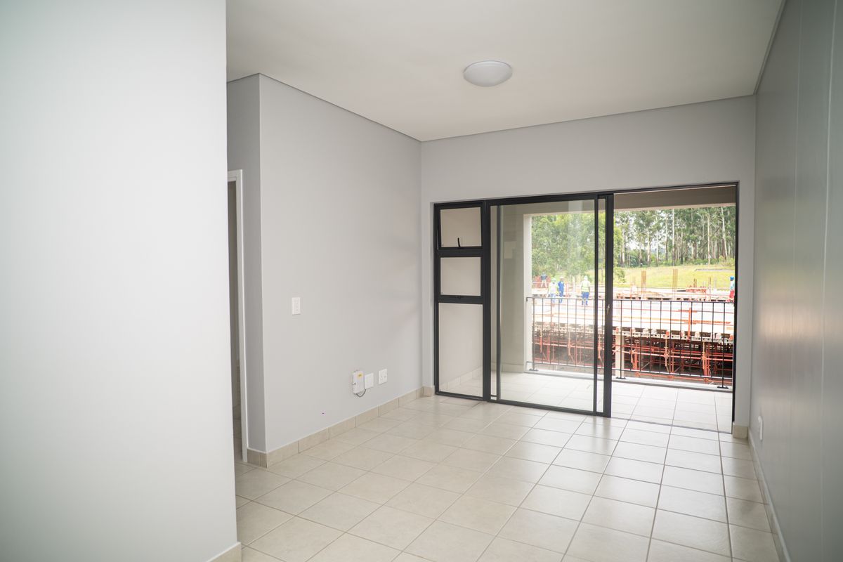A bright, empty living area featuring neutral tiled flooring and large sliding glass doors that open onto a private balcony.