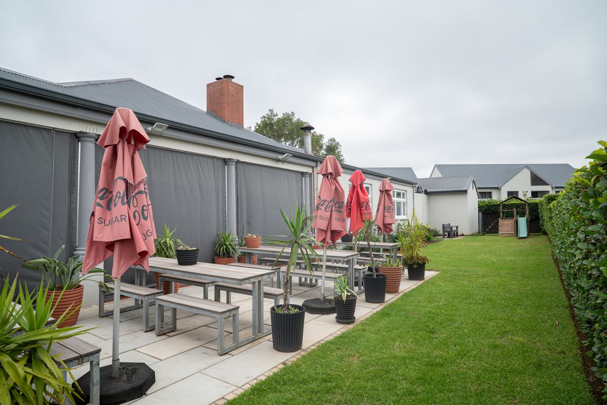 A spacious rear patio area featuring paved flooring, retractable outdoor blinds, and a well-maintained lawn, ideal for outdoor entertaining.