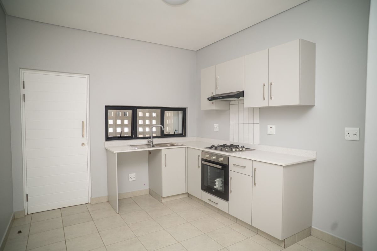 A clean, modern kitchen featuring light-toned cabinetry, a built-in gas hob, oven, extractor fan, and a stainless steel sink with tiled flooring.