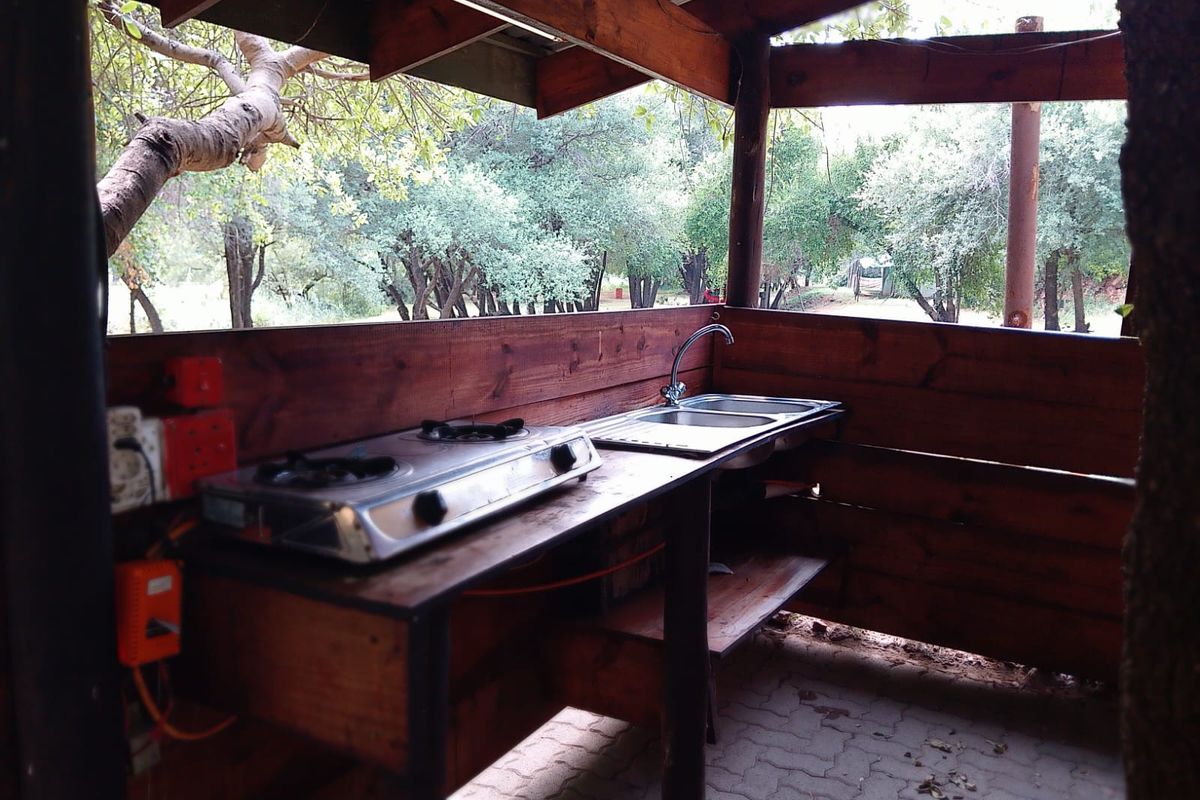 Outdoor kitchen area featuring a built-in timber counter, stainless steel sink, and gas hob, set within a rustic covered structure.