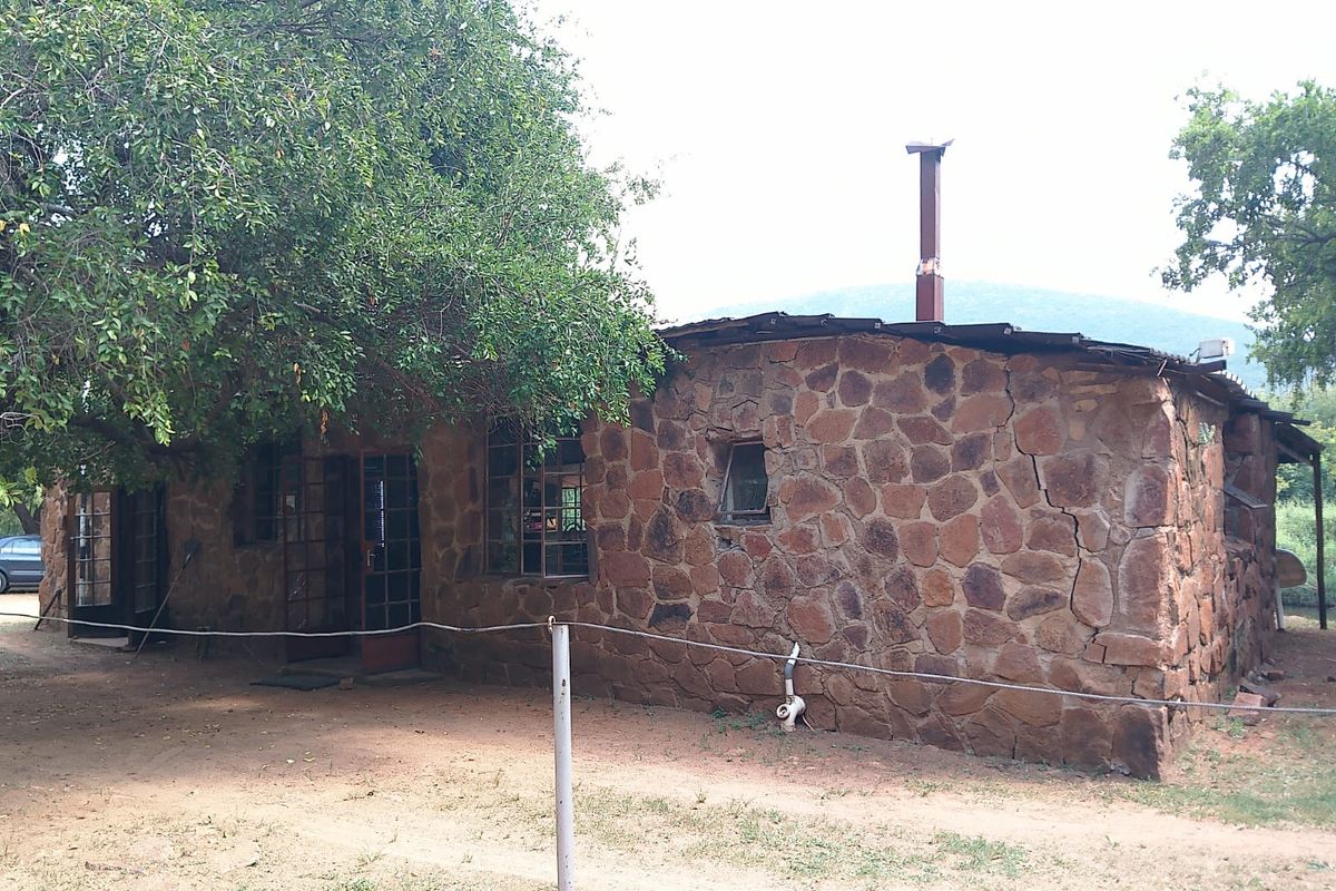 Rustic stone-clad farm building featuring a chimney stack and metal-framed windows, set within a natural landscape.
