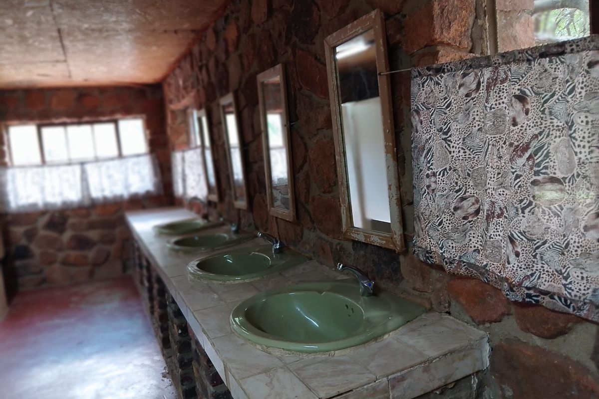 A rustic bathroom facility featuring multiple built-in vanity basins set into a stone-clad counter with exposed brickwork and wall-mounted mirrors.