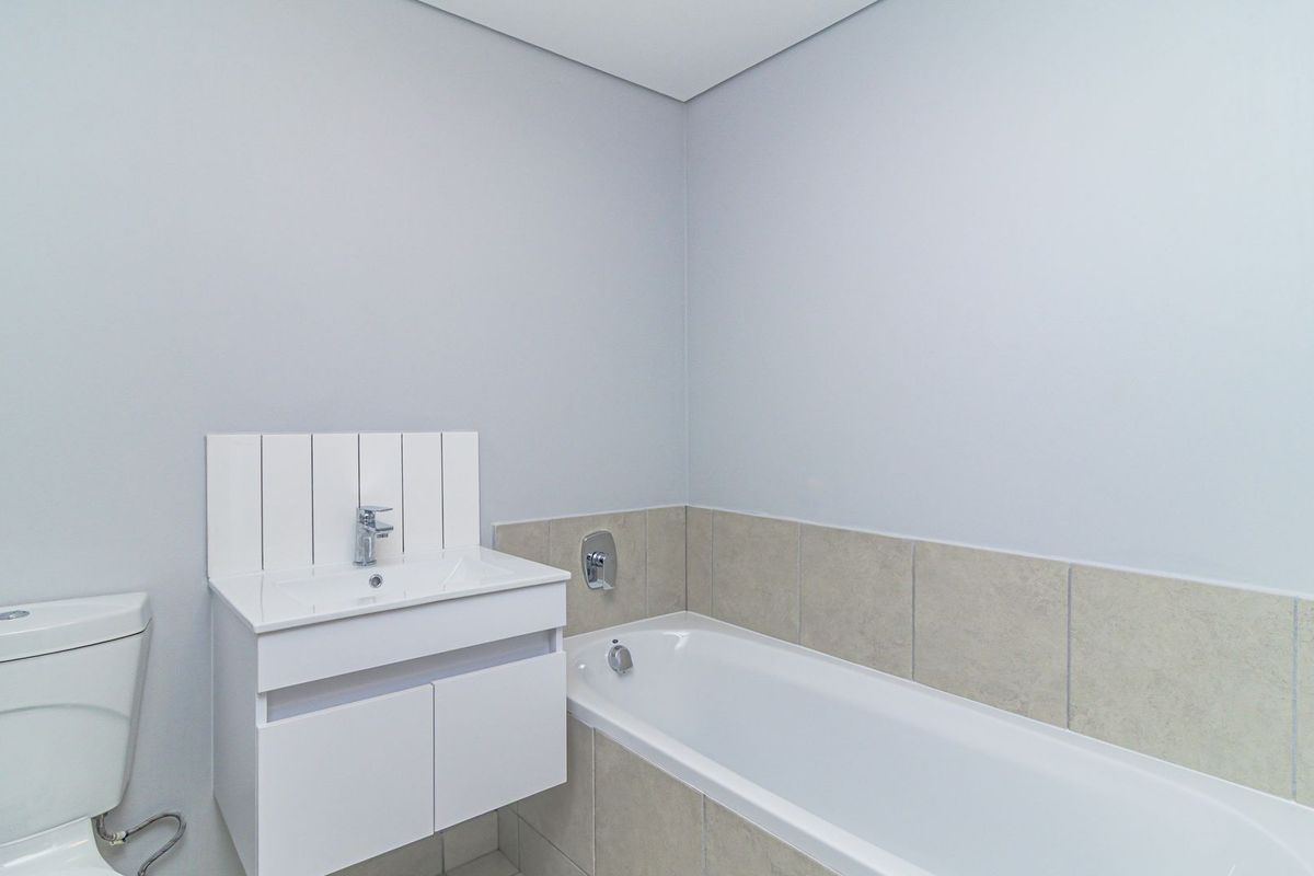 A clean, modern bathroom featuring a white vanity with integrated basin, a bathtub with neutral wall tiling, and a standard toilet.