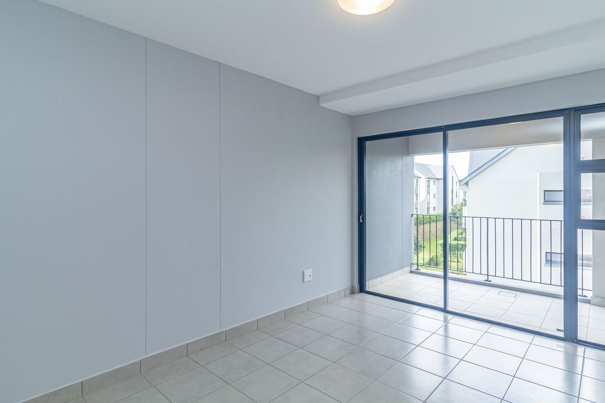 A bright, empty bedroom featuring neutral tiled flooring, smooth walls, and large sliding glass doors that open onto a private balcony.