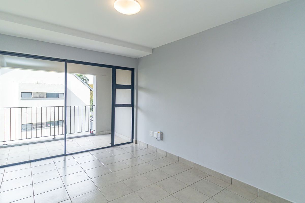 An empty living room featuring neutral tiled flooring, a ceiling light fixture, and large sliding glass doors leading to a private balcony.