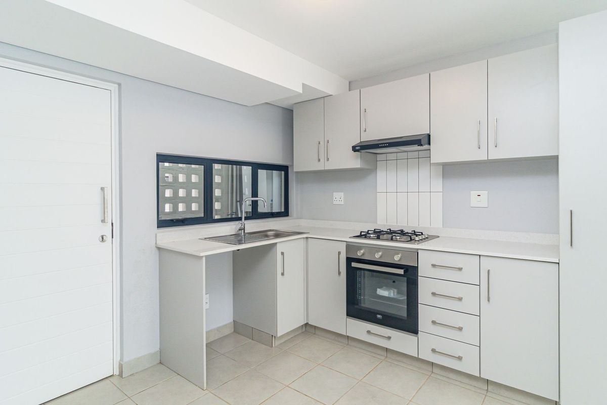A clean, modern kitchen featuring light grey cabinetry, stone-look countertops, a built-in gas hob, oven, extractor fan, and a stainless steel sink.