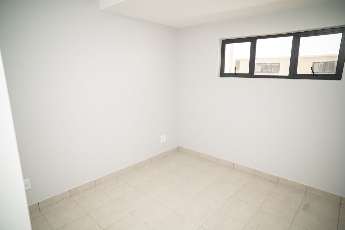 A clean, empty bedroom featuring neutral tiled flooring, light-colored walls, and a modern dark-framed window.
