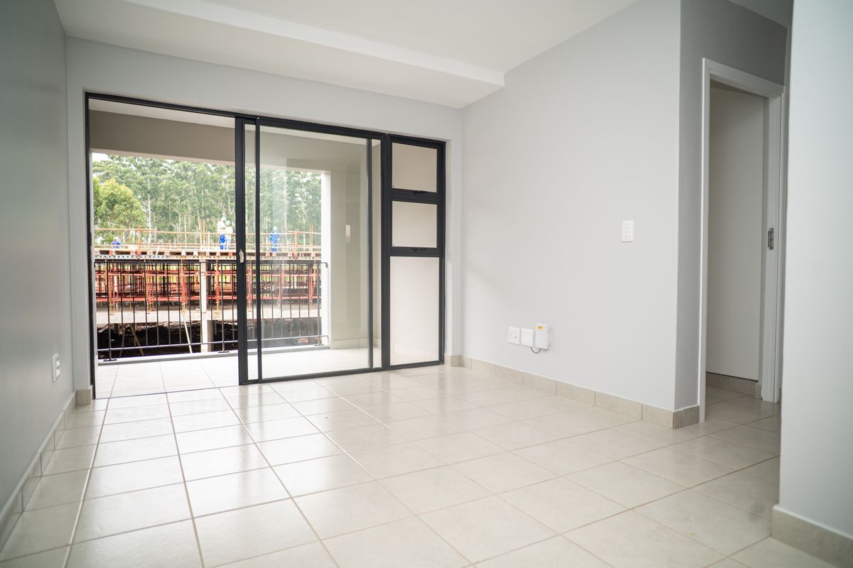 An empty living room featuring neutral tiled flooring and large sliding glass doors that open onto a balcony.