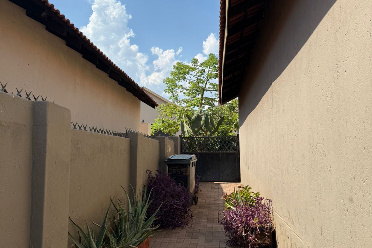 A narrow side passage featuring paved flooring, perimeter boundary walls, and tiled roof eaves, providing access between two sections of the property.