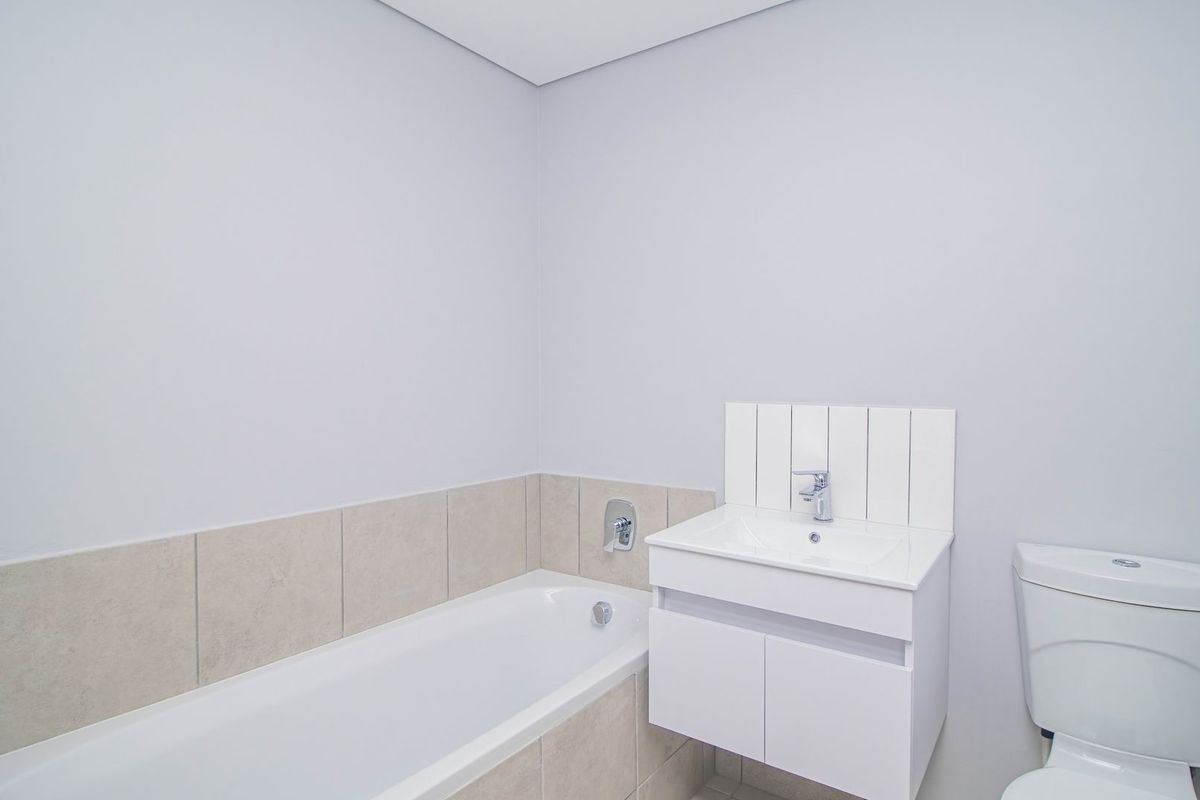 A clean and modern bathroom featuring a white vanity with integrated basin, a bathtub with tiled surround, and a standard toilet.