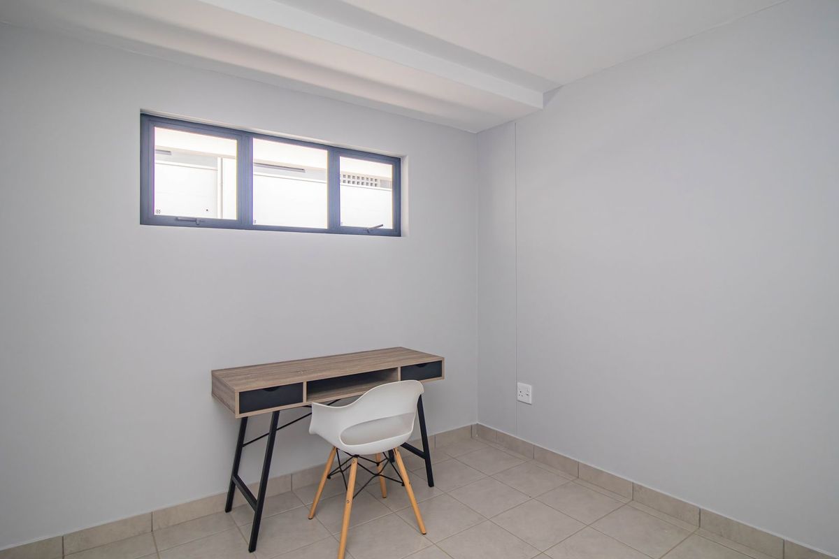 A clean, neutral-toned room featuring tiled flooring and a high-set horizontal window, suitable for use as a home office or bedroom.