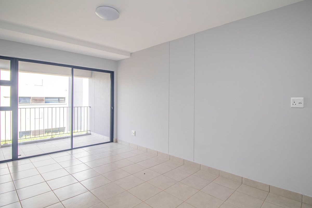 A bright, empty living room featuring neutral tiled flooring, a modern ceiling light, and large sliding glass doors leading to a private balcony.