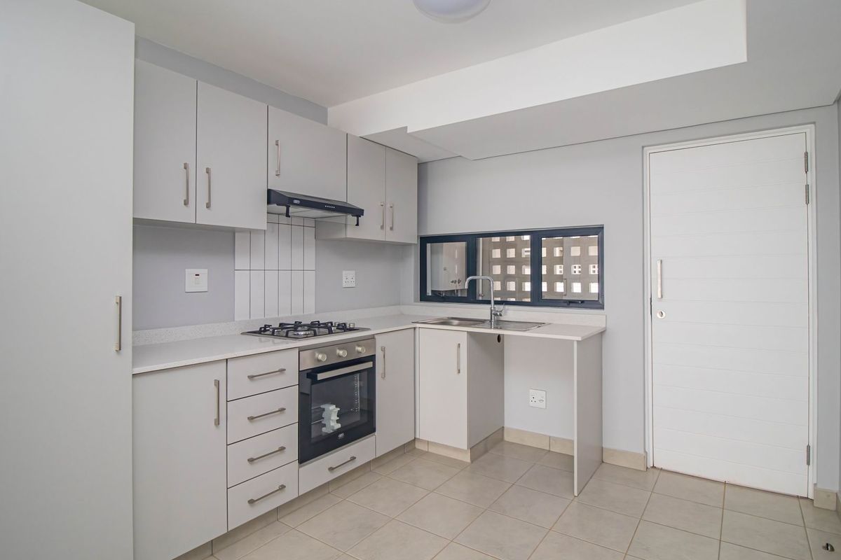 A modern, clean kitchen featuring light grey cabinetry, a built-in oven, gas hob, extractor fan, and tiled flooring.