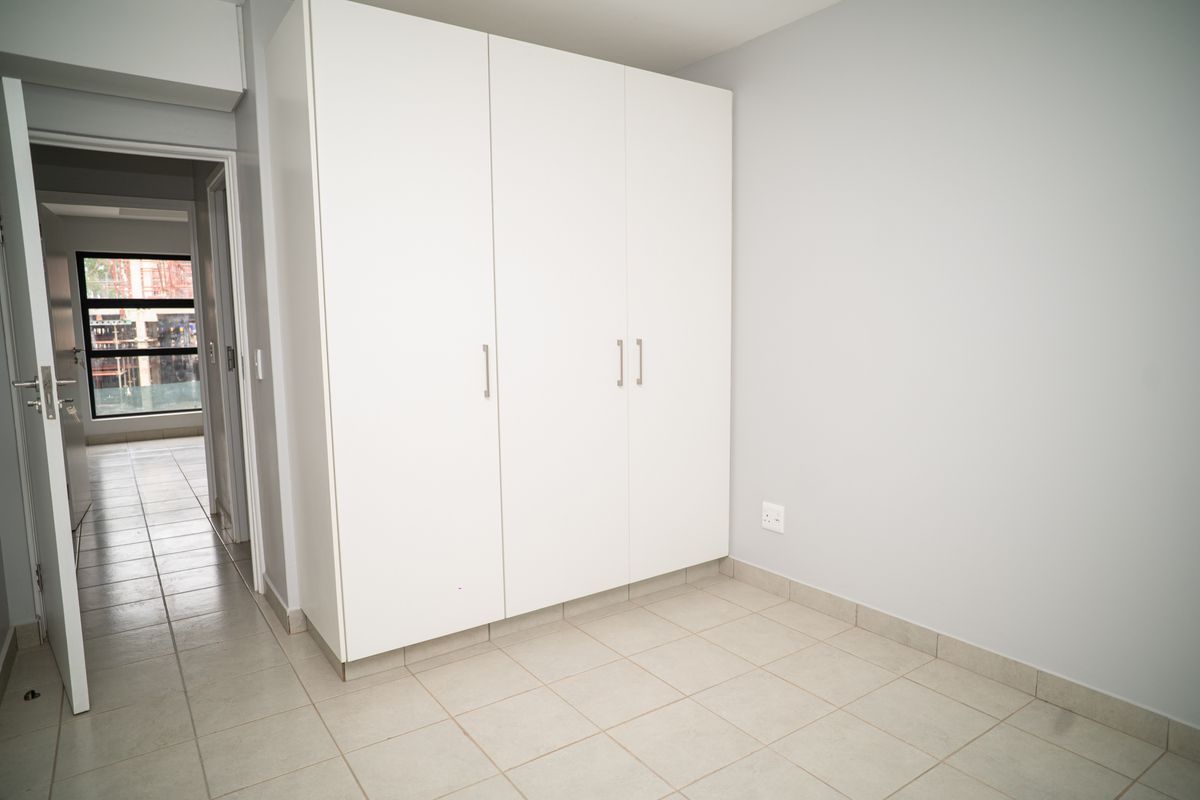 A bright bedroom featuring neutral tiled flooring and built-in white cabinetry, offering a clean and minimalist space.
