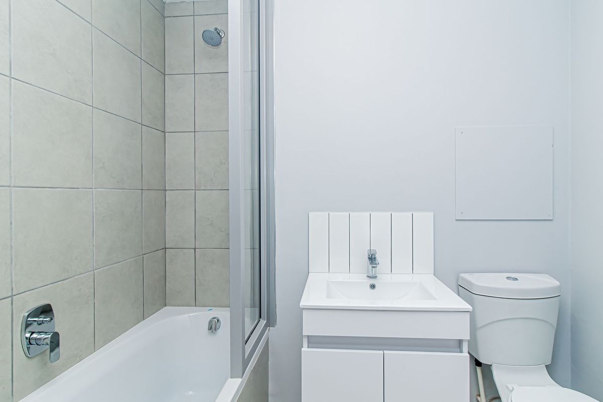 A clean, functional bathroom featuring a shower-over-bath combination, a modern white vanity with basin, and a standard toilet.