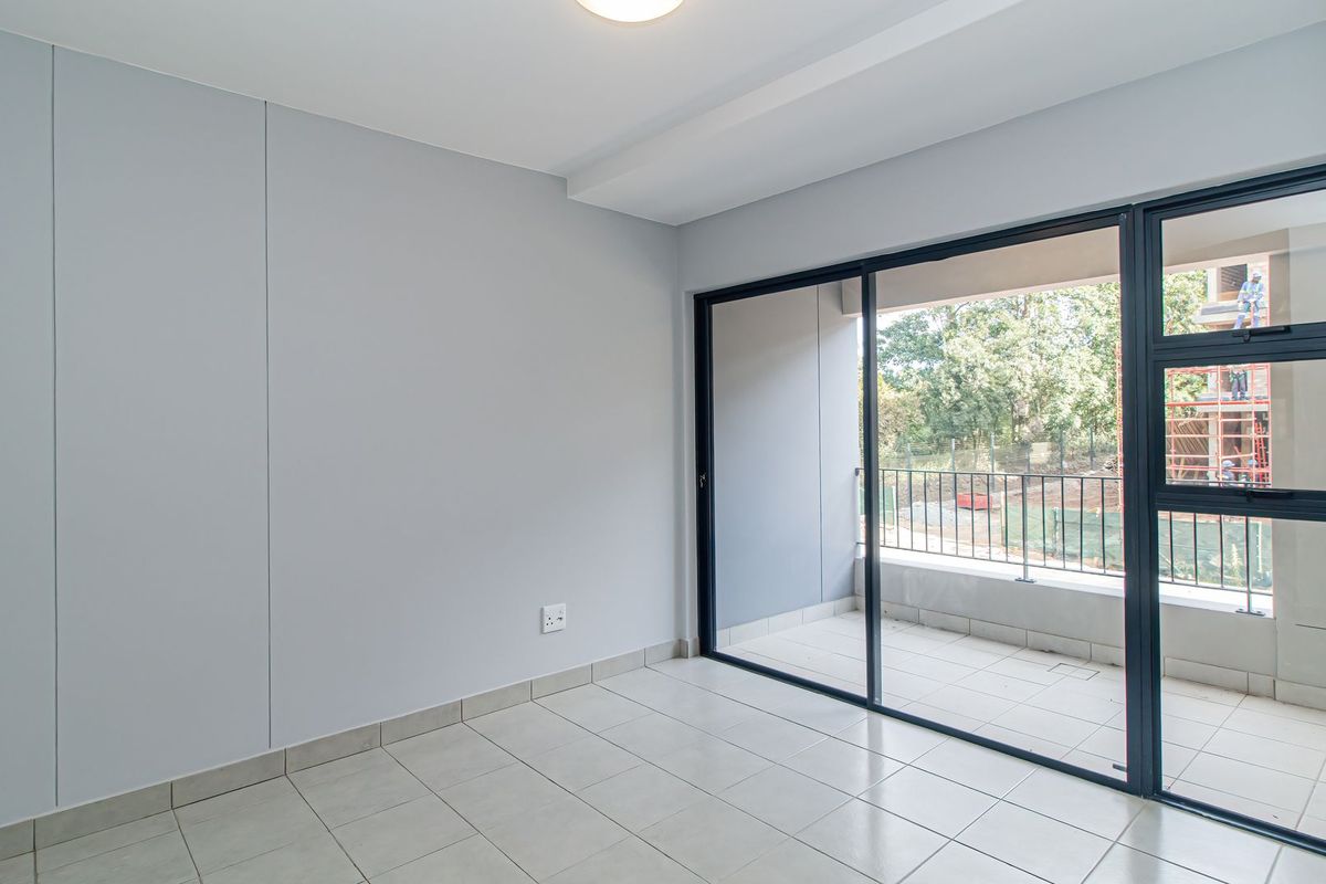 A bright, empty bedroom featuring neutral tiled flooring, smooth grey walls, and large sliding glass doors that open onto a private balcony.