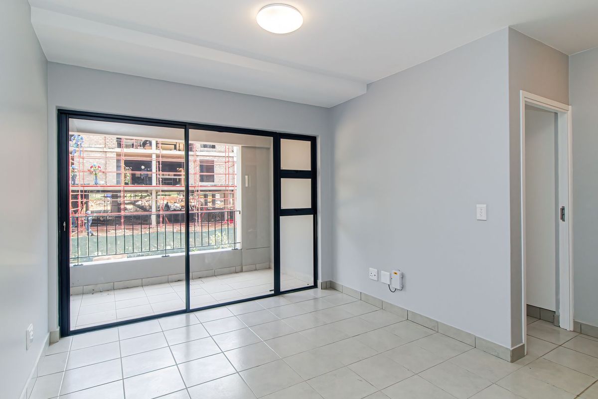 A bright, empty living area featuring neutral tiled flooring and large sliding glass doors that open onto a private balcony.