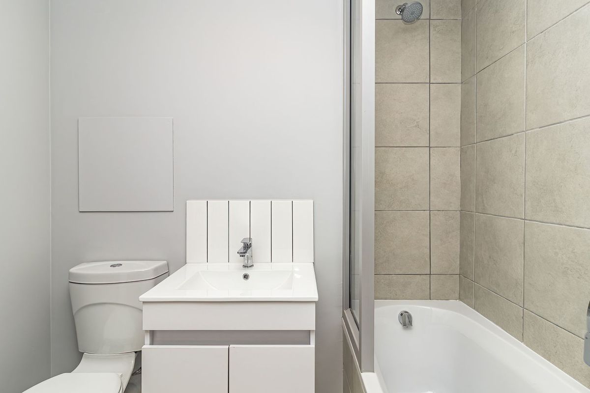 A clean, modern bathroom featuring a white vanity, a combined shower and bathtub unit with neutral wall tiling, and a standard toilet.