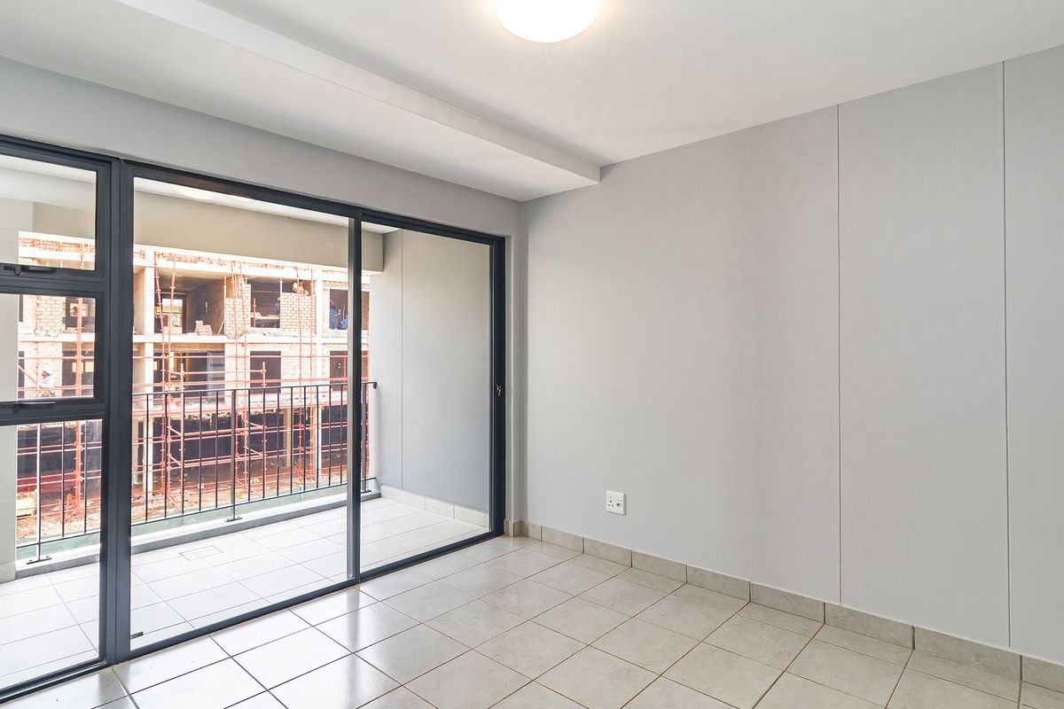 A bright, empty bedroom featuring tiled flooring, neutral walls, and large sliding glass doors that open onto a private balcony.