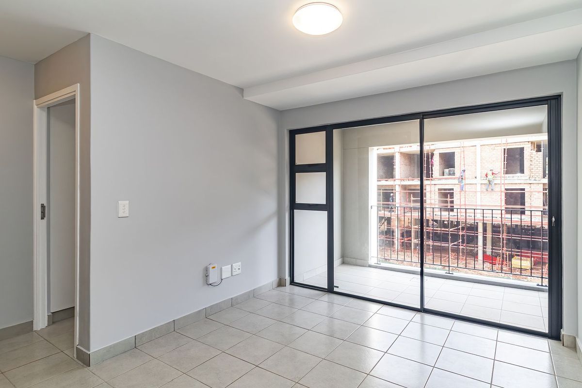 A bright, empty living area featuring neutral tiled flooring, modern grey walls, and large sliding glass doors opening onto a private balcony.