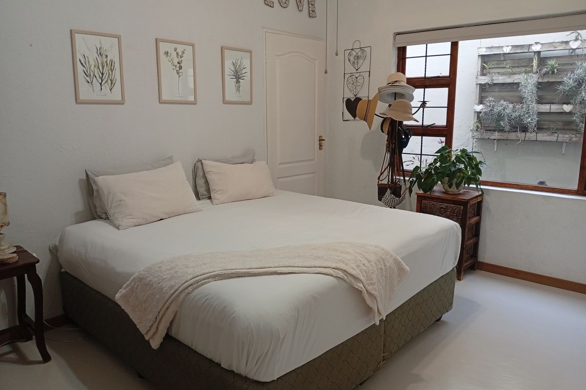 A bedroom featuring a large bed, smooth flooring, and a window overlooking a small outdoor garden area with vertical wooden planters.