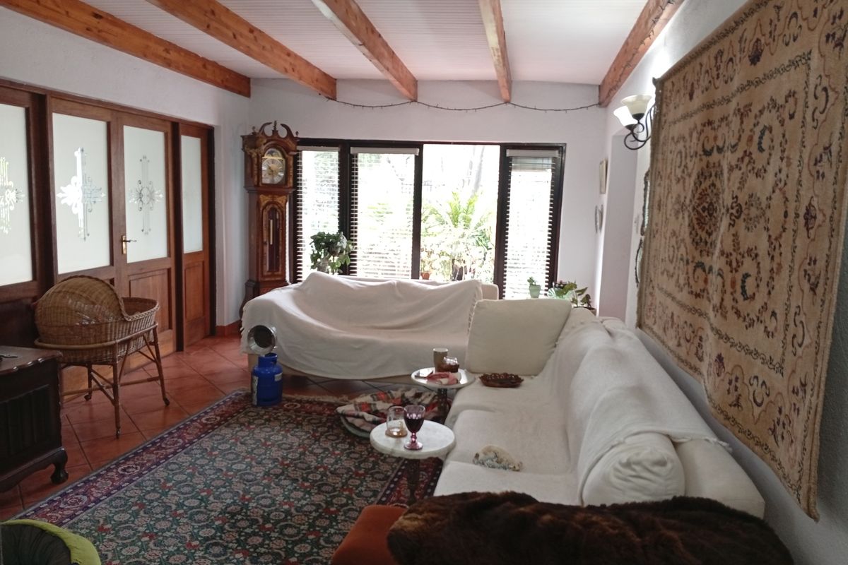 Spacious living room featuring exposed timber ceiling beams, terracotta floor tiles, and large sliding glass doors providing natural light and garden access.