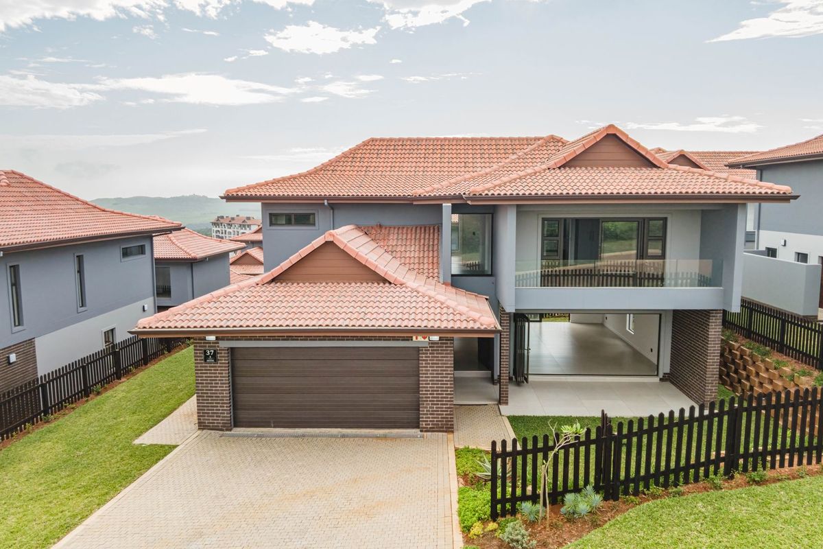 Aerial view of a modern double-story residential home featuring a tiled roof, brick and plaster facade, double garage, and a paved driveway.