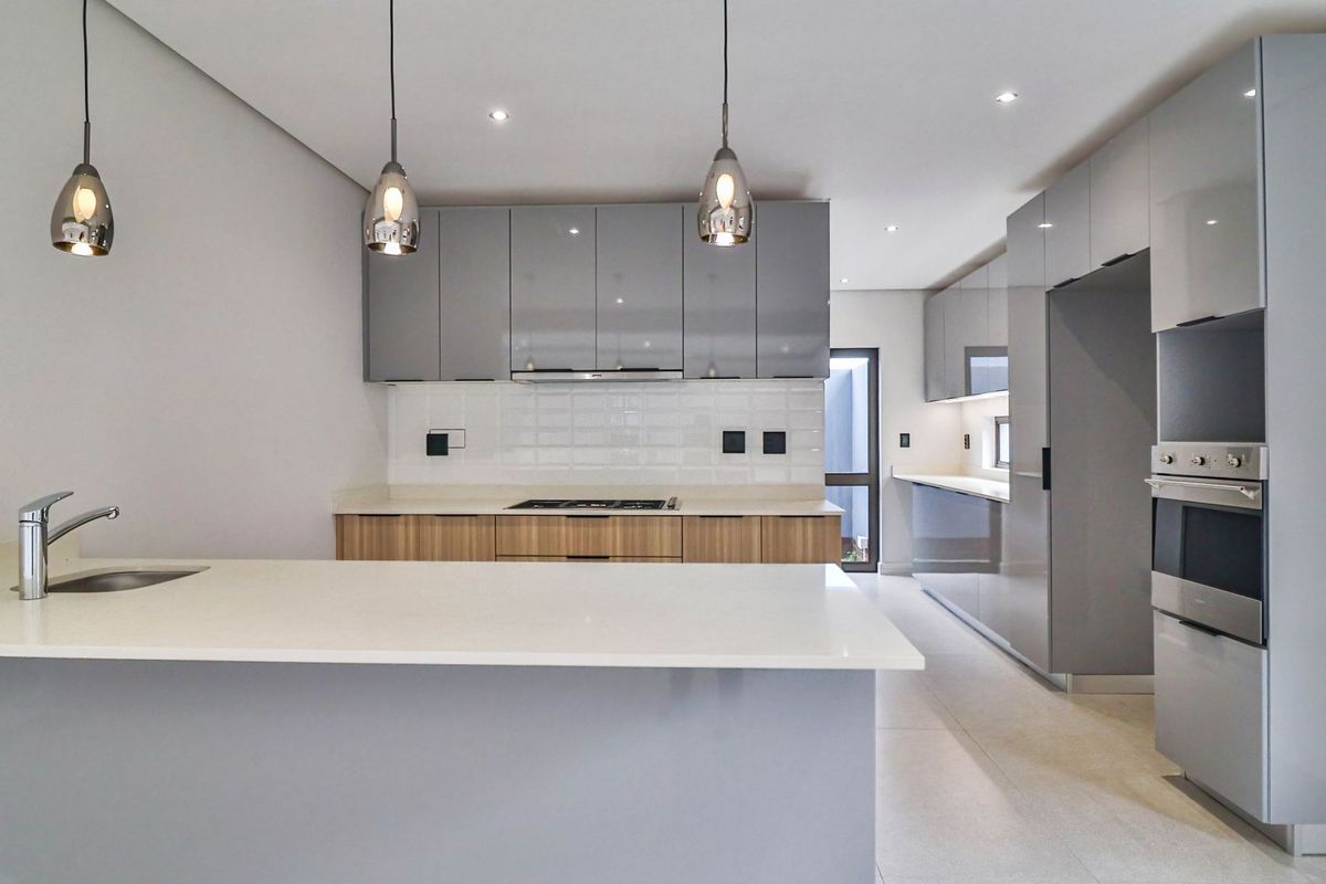 Modern kitchen featuring sleek grey cabinetry, stone countertops, a central island with a sink, and integrated stainless steel appliances.