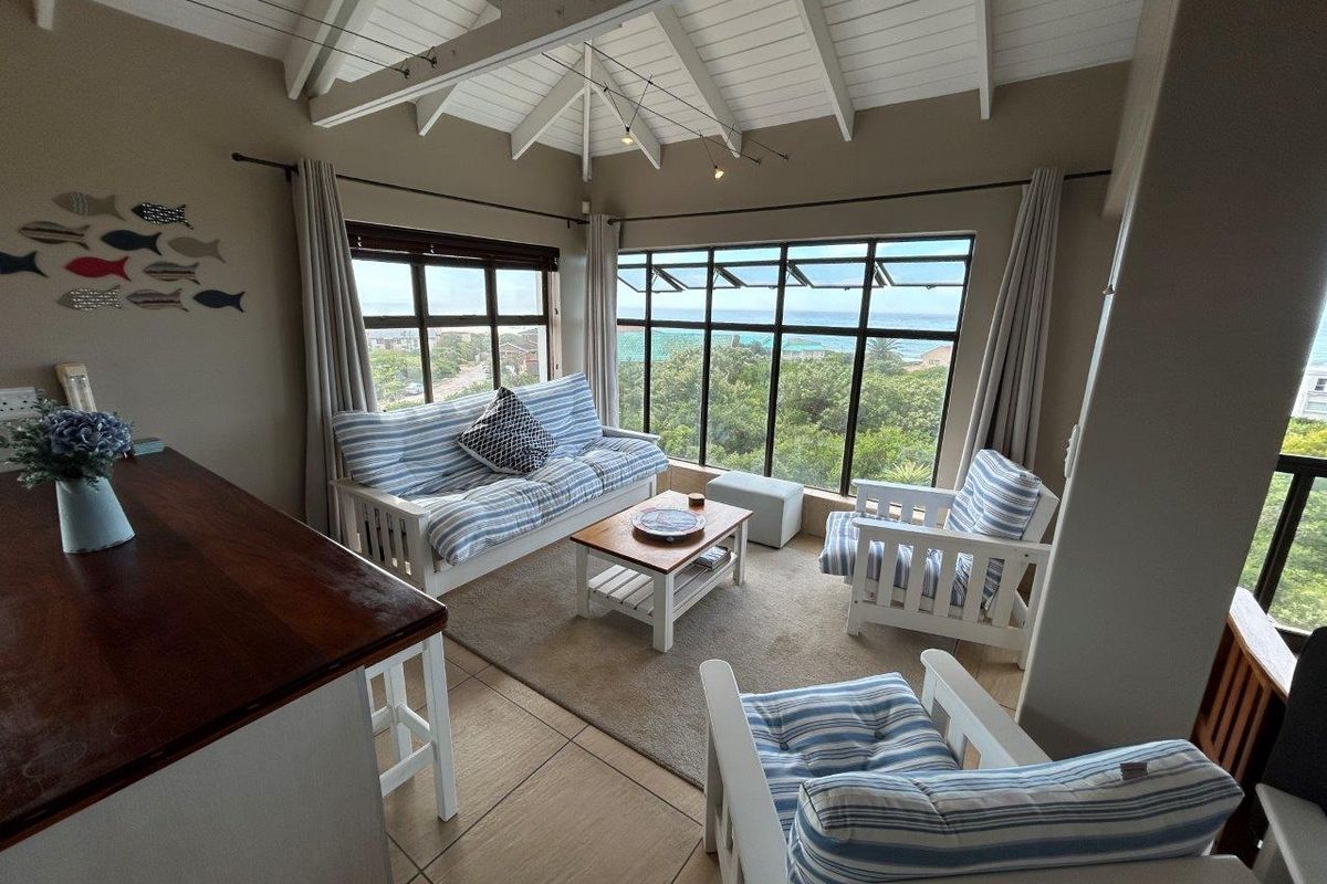 A bright living area featuring vaulted ceilings, large windows with scenic coastal views, and tiled flooring.
