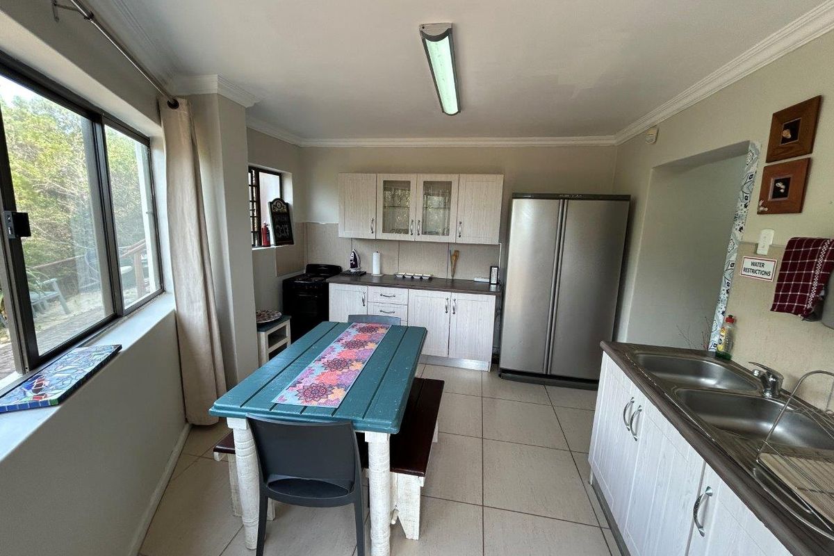 A functional kitchen featuring light-toned cabinetry, tiled flooring, a double stainless steel sink, and a dedicated dining area with large windows.