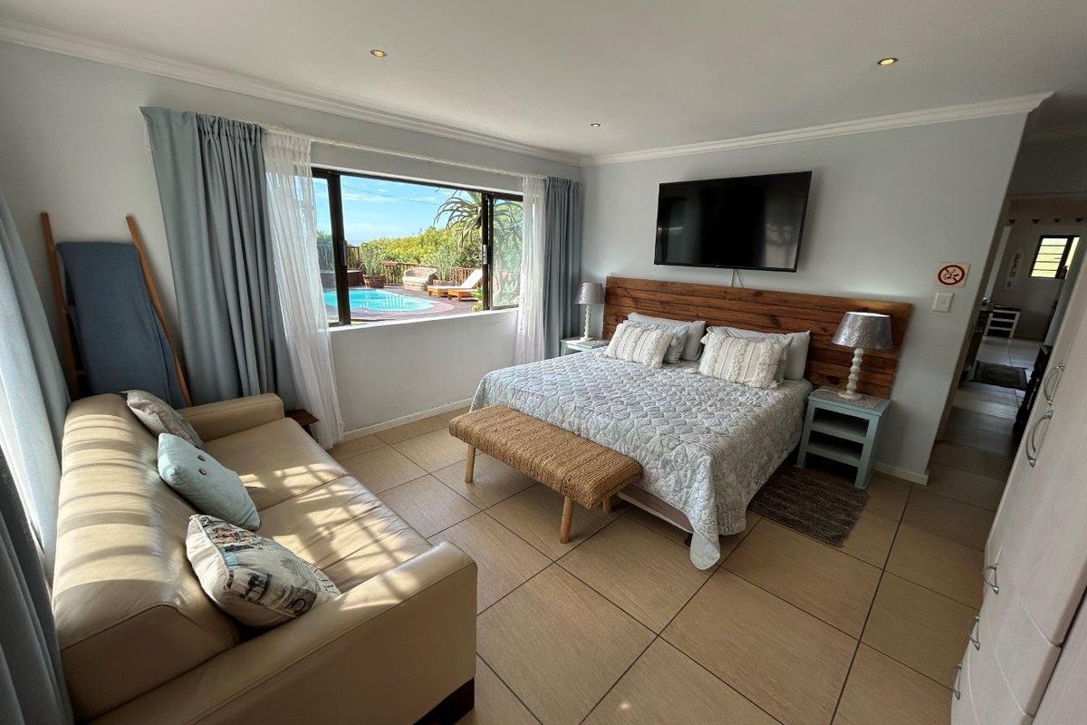 Spacious bedroom featuring large format floor tiles, a custom timber headboard, and a large window offering views of the outdoor pool area.