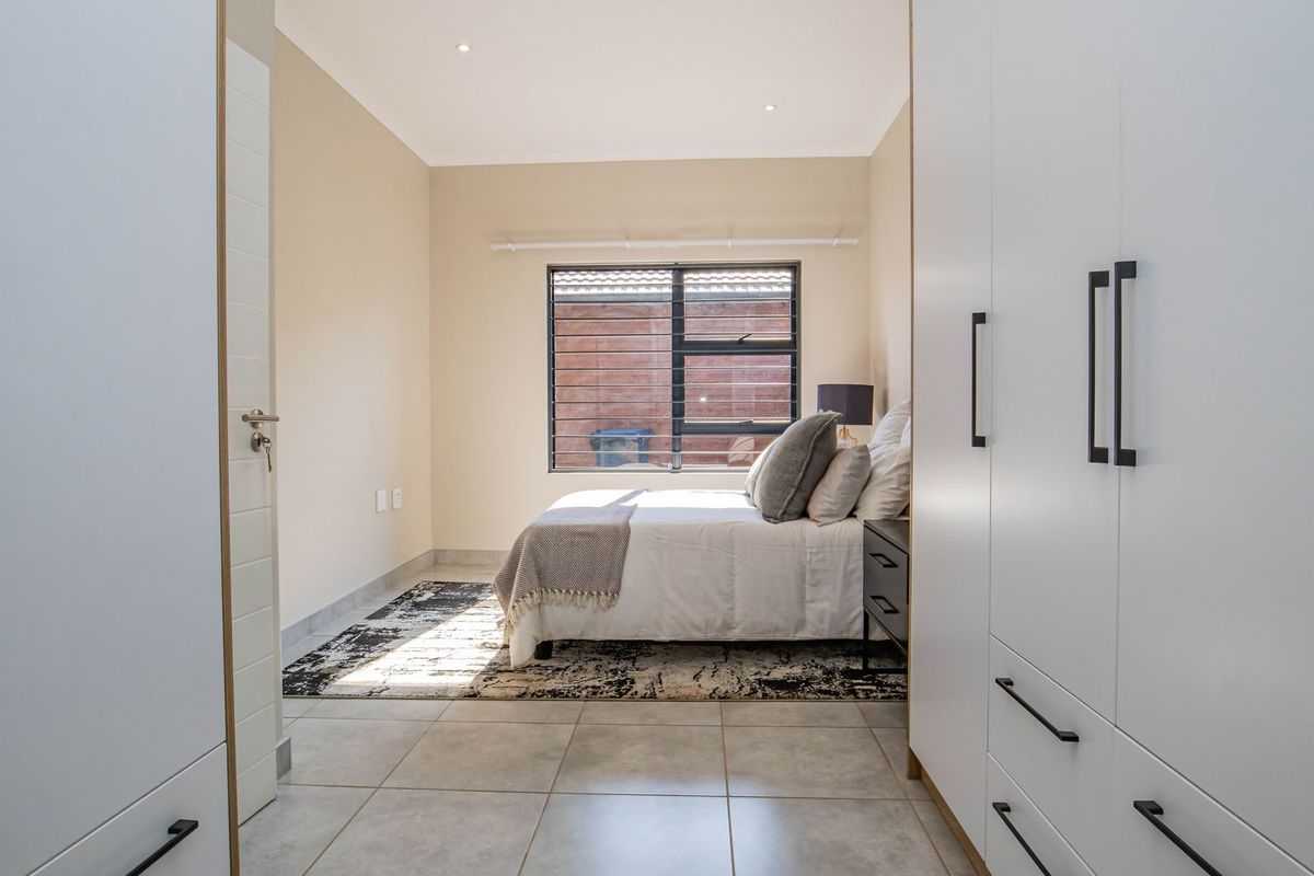 A bright bedroom featuring neutral tiled flooring, built-in floor-to-ceiling cabinetry, and a window with security bars.
