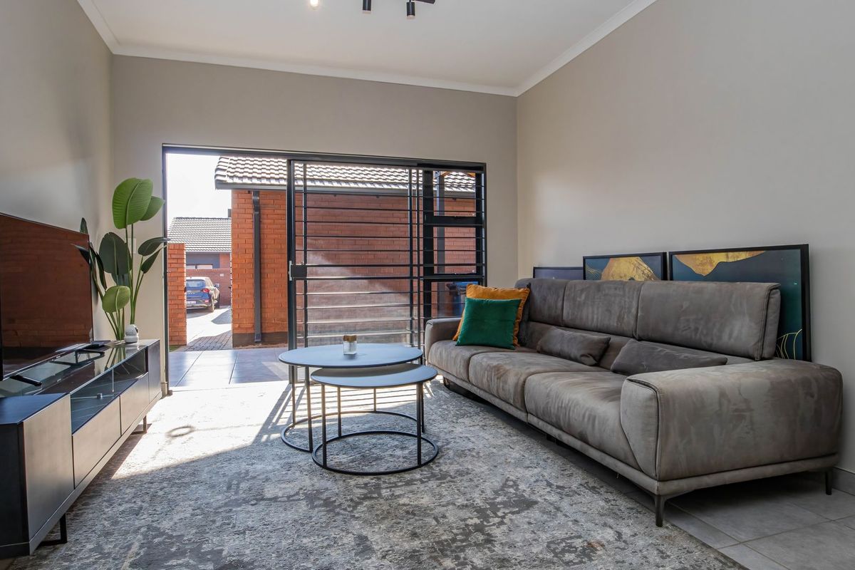 A bright living room featuring tiled flooring, neutral walls, and a large sliding door providing direct access to the exterior paved area.