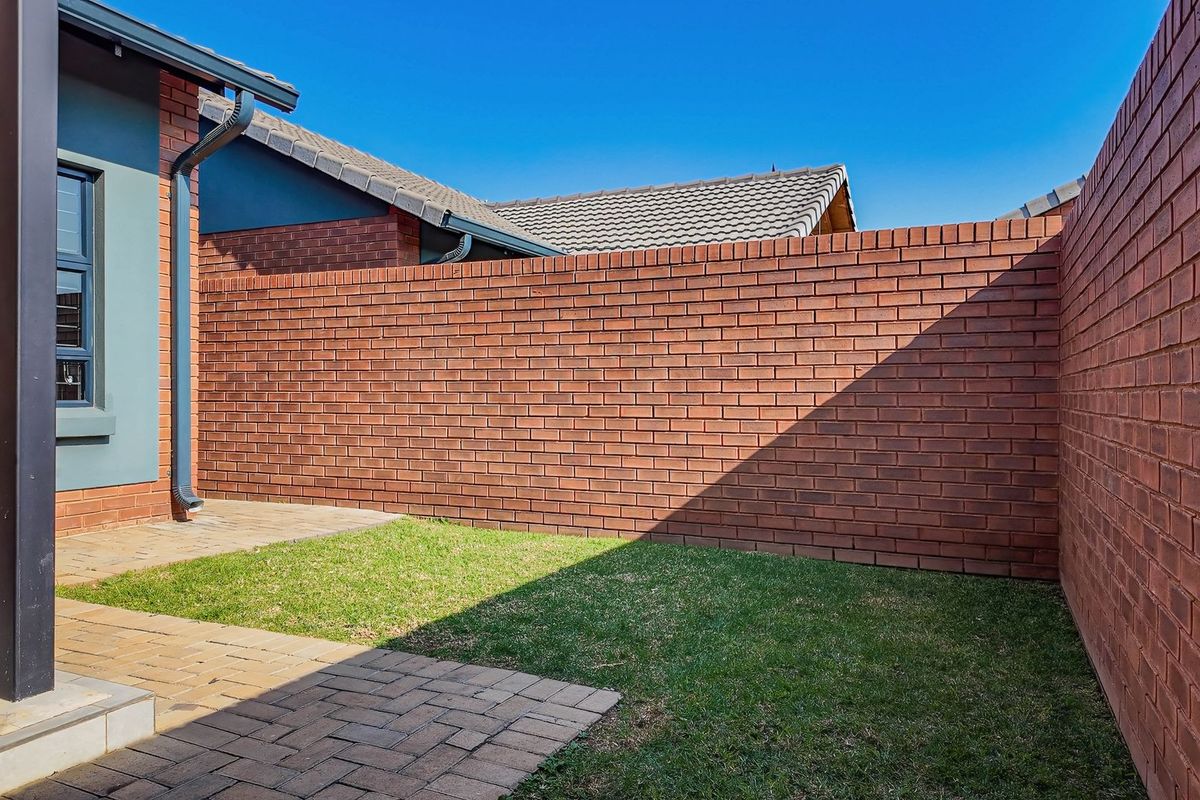 A private rear courtyard featuring a paved patio area, a small lawn, and high perimeter brick boundary walls for added privacy.