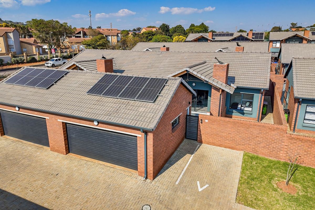 Aerial view of a townhouse featuring a double garage, brick facade, tiled roof, and installed solar panels.